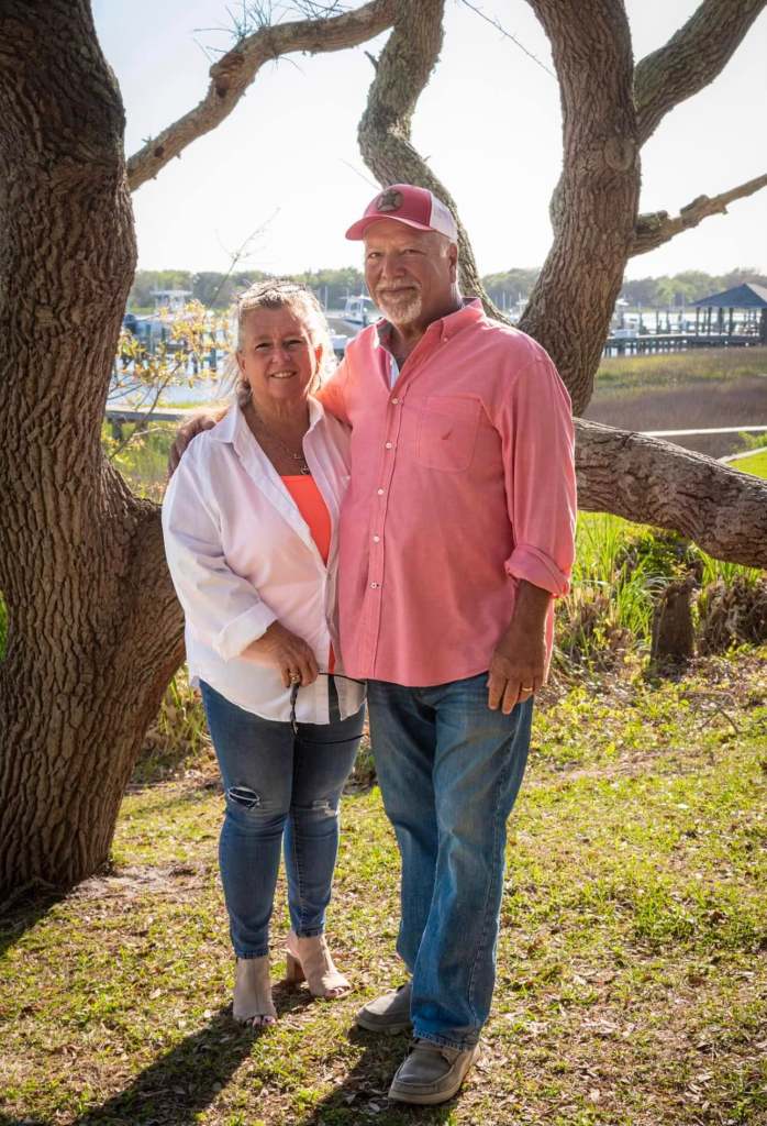 A woman and man standing next to each other with trees behind them. 