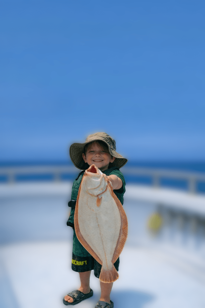 Kid holding big summer flounder with blurry boat in the background